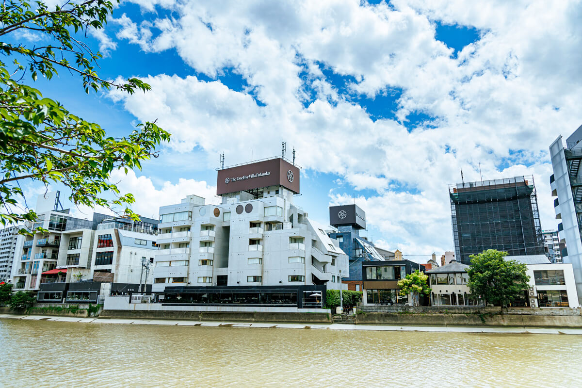 中洲側から⾒た「ザ・ワンファイブヴィラ福岡」(⼿前)と「ザ・ワンファイブテラス福岡」(奥)、⼯事中の「ホテル イル・パラッツォ」(右側)(2023年7⽉撮影)